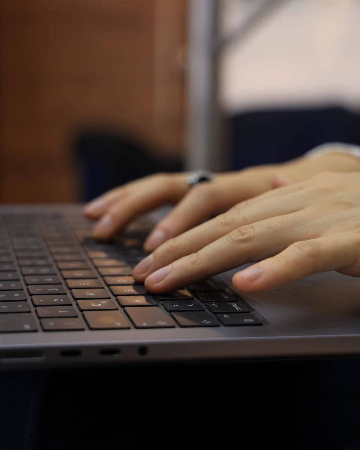 Hands resting on a laptop keyboard in low light, the screen turned away from the camera.