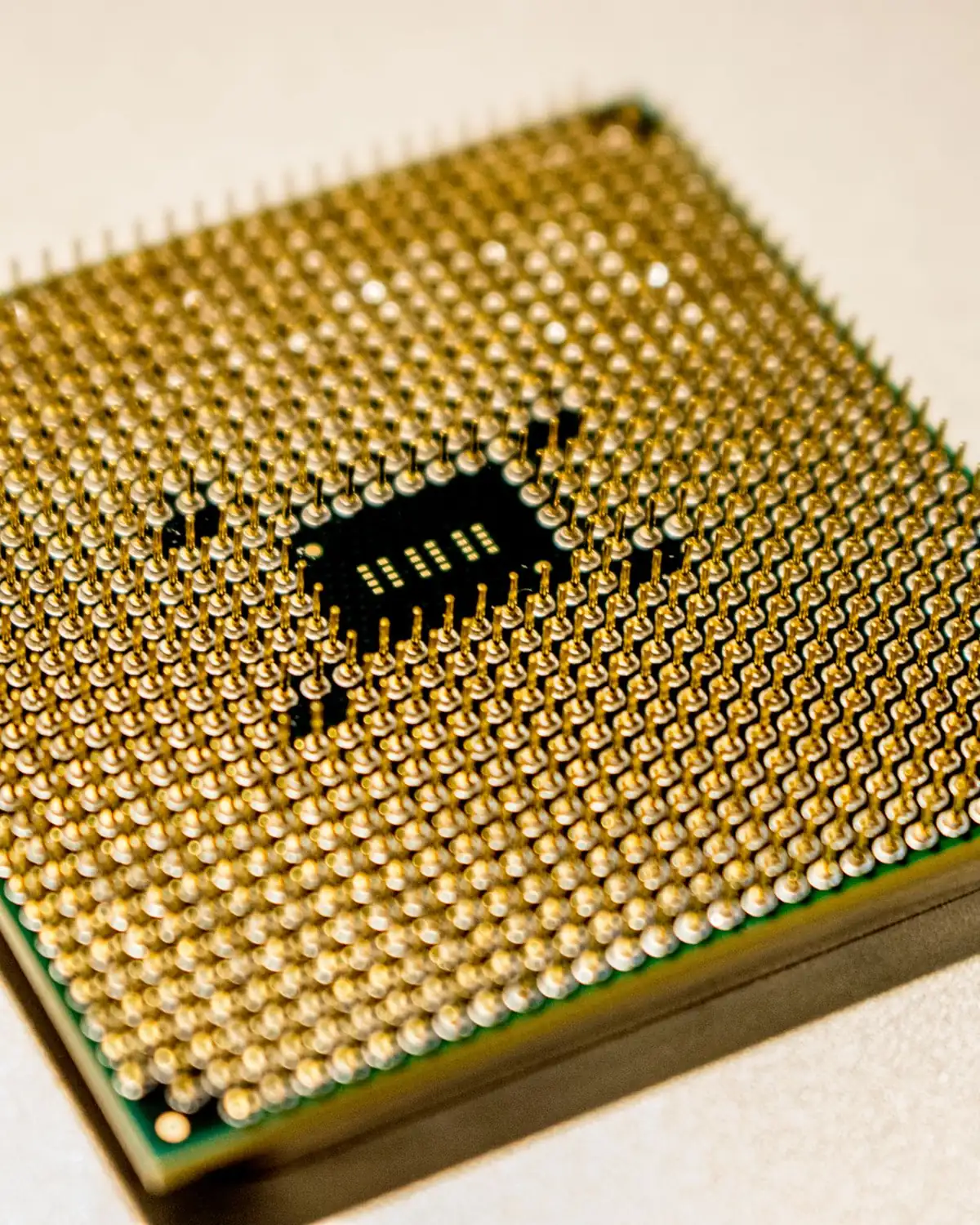 A computer processor chip with a gold pin grid resting on a pale surface.