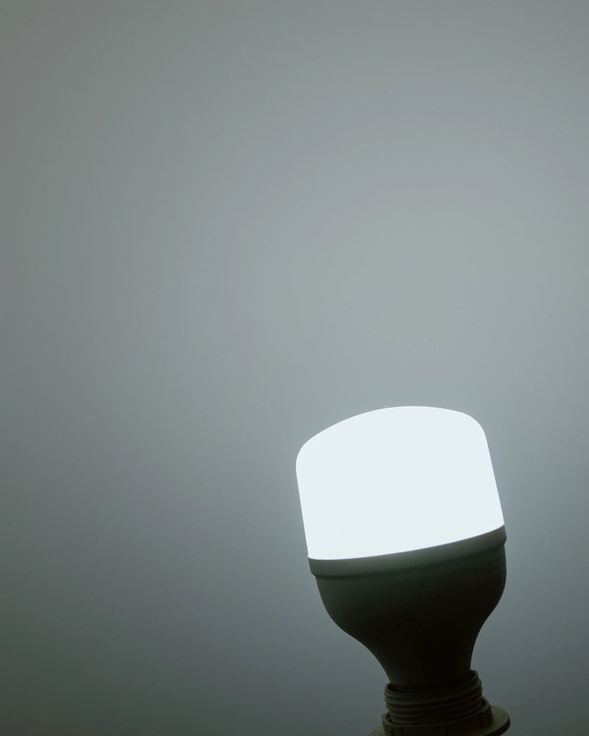 A modern LED lamp glowing on its holder against a plain dark background.