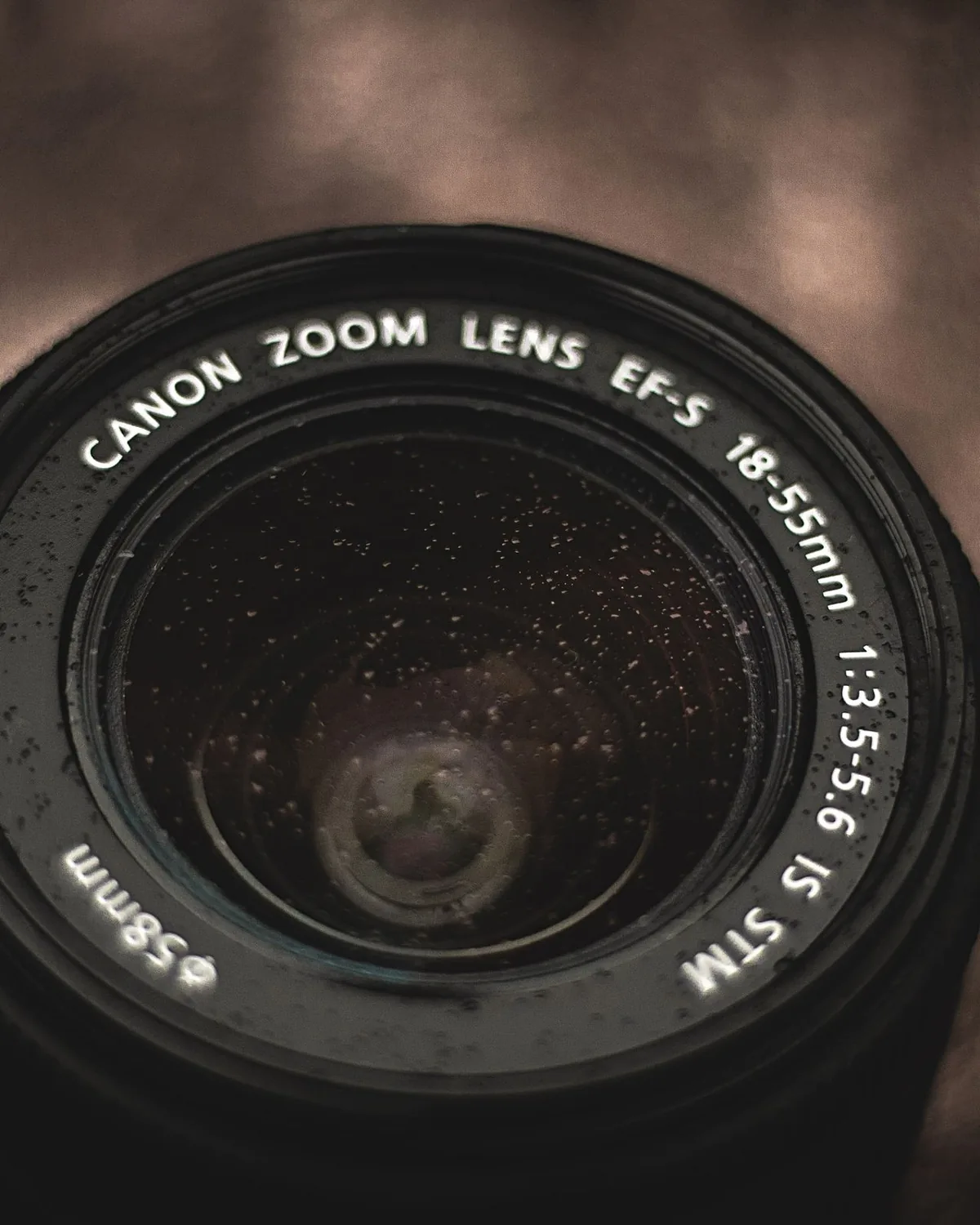 Close view of a camera lens front element and focus ring, markings visible around the barrel.