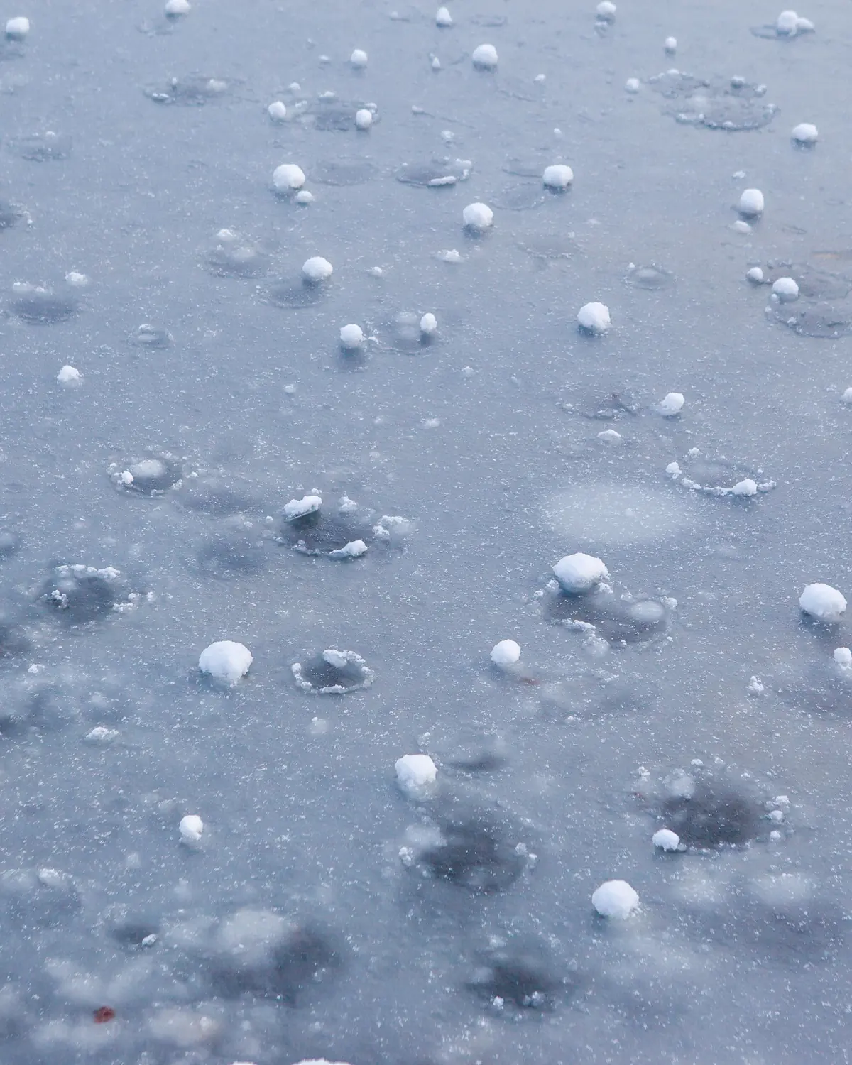 Hailstones scattered across wet icy ground after heavy rain.