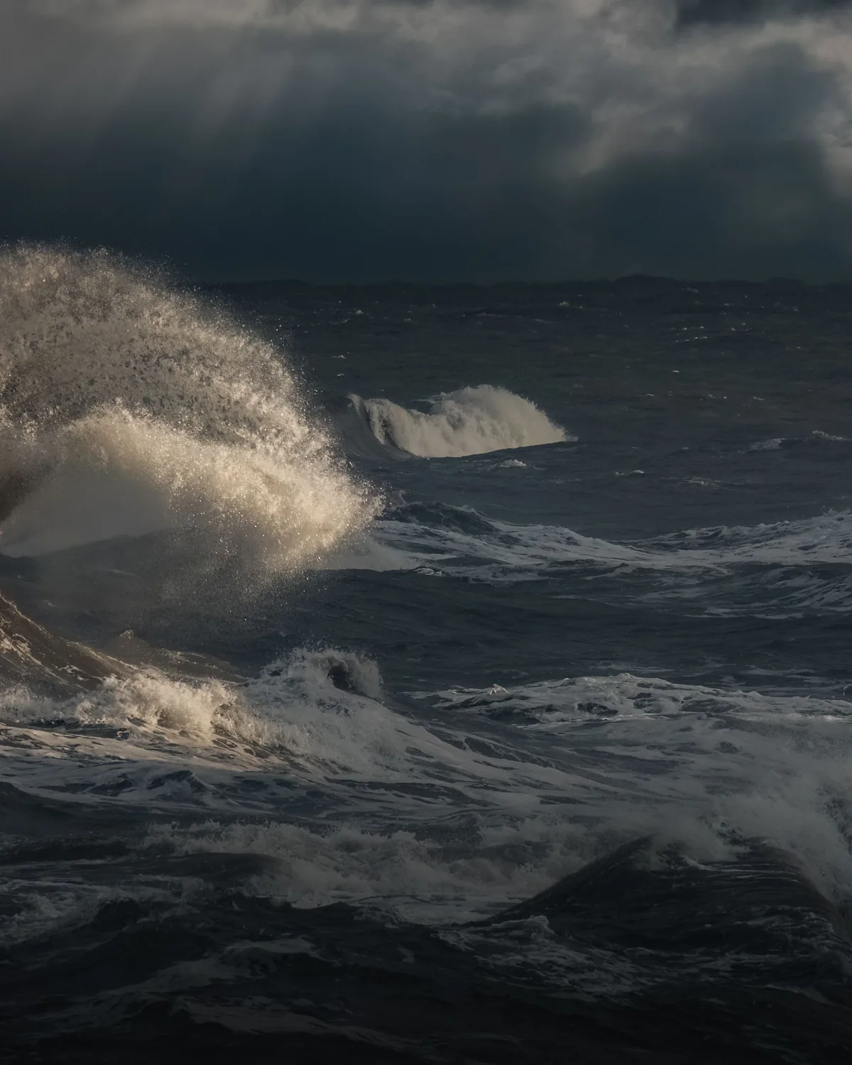 Wind-driven swell and spray on an open sea under heavy dark cloud.