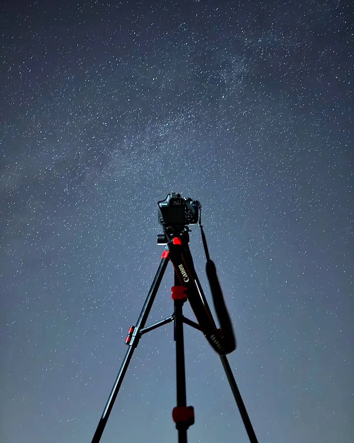 A camera on a tripod set up outdoors at night framed against a dark starry sky.