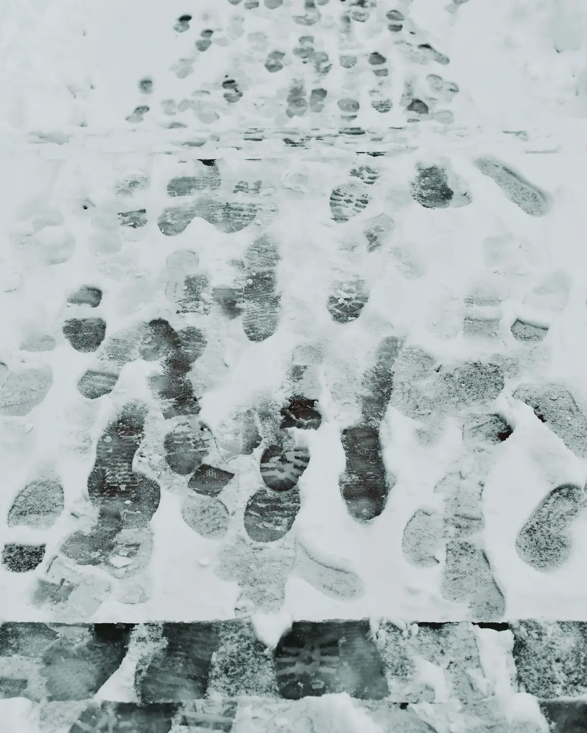 Footprints pressed into a frozen glazed layer of ice and packed snow on a pavement.