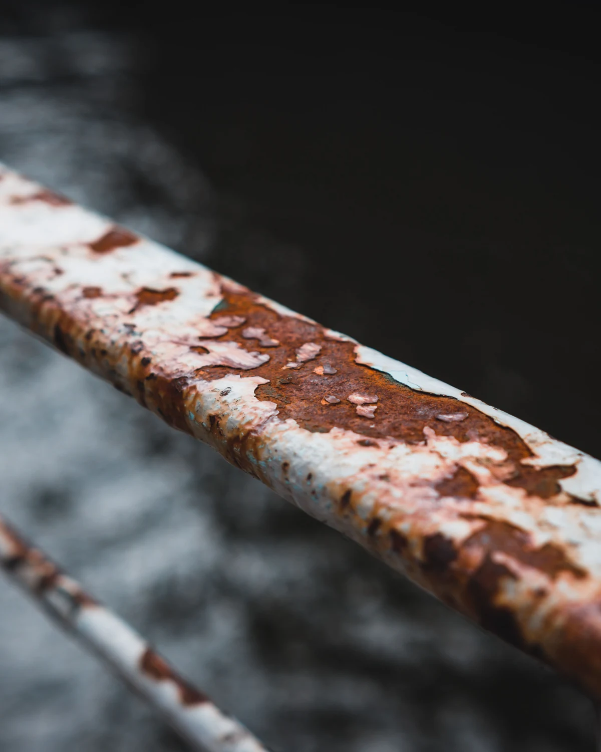 Orange-brown rust spreading along a metal railing above dark water.