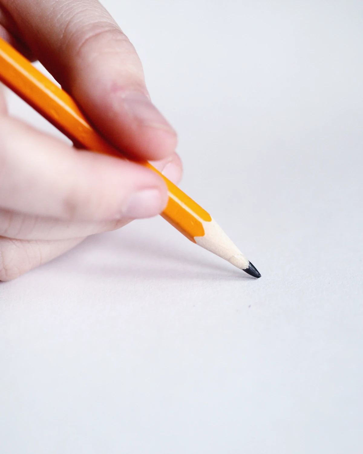 A hand holding a yellow wooden pencil and writing on a sheet of white paper.
