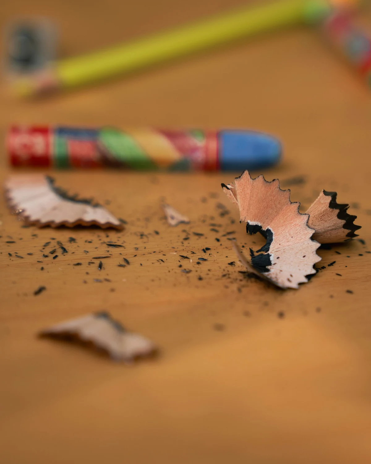 Curled pencil shavings and a small sharpener beside pencils on a pale wooden desk.