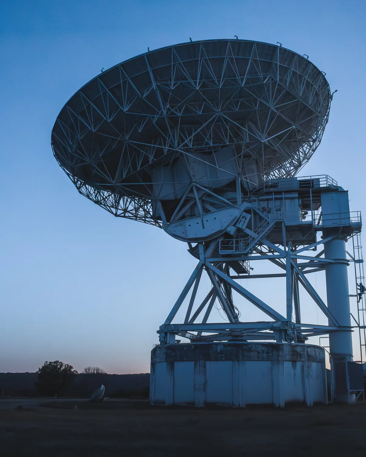 A large steel radio telescope dish tilted toward a darkening twilight sky.