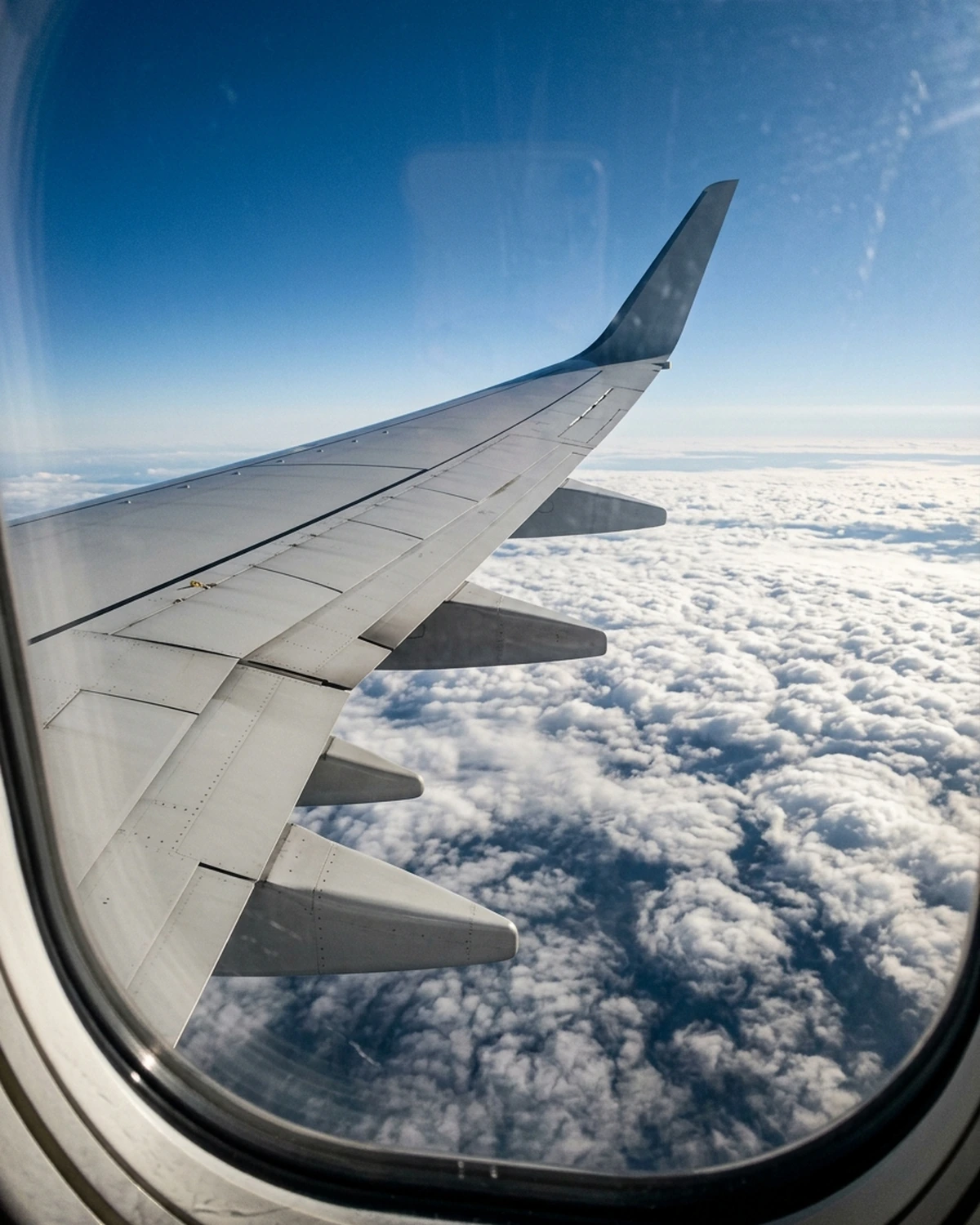 A swept passenger-aircraft wing seen through a window above a cloud layer during cruise